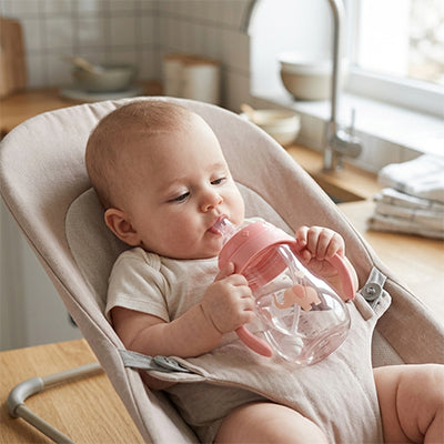 Bébé avec biberon rose dans son transat dans la cuisine