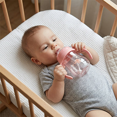 Bébé couché dans bassinette avec biberon rose