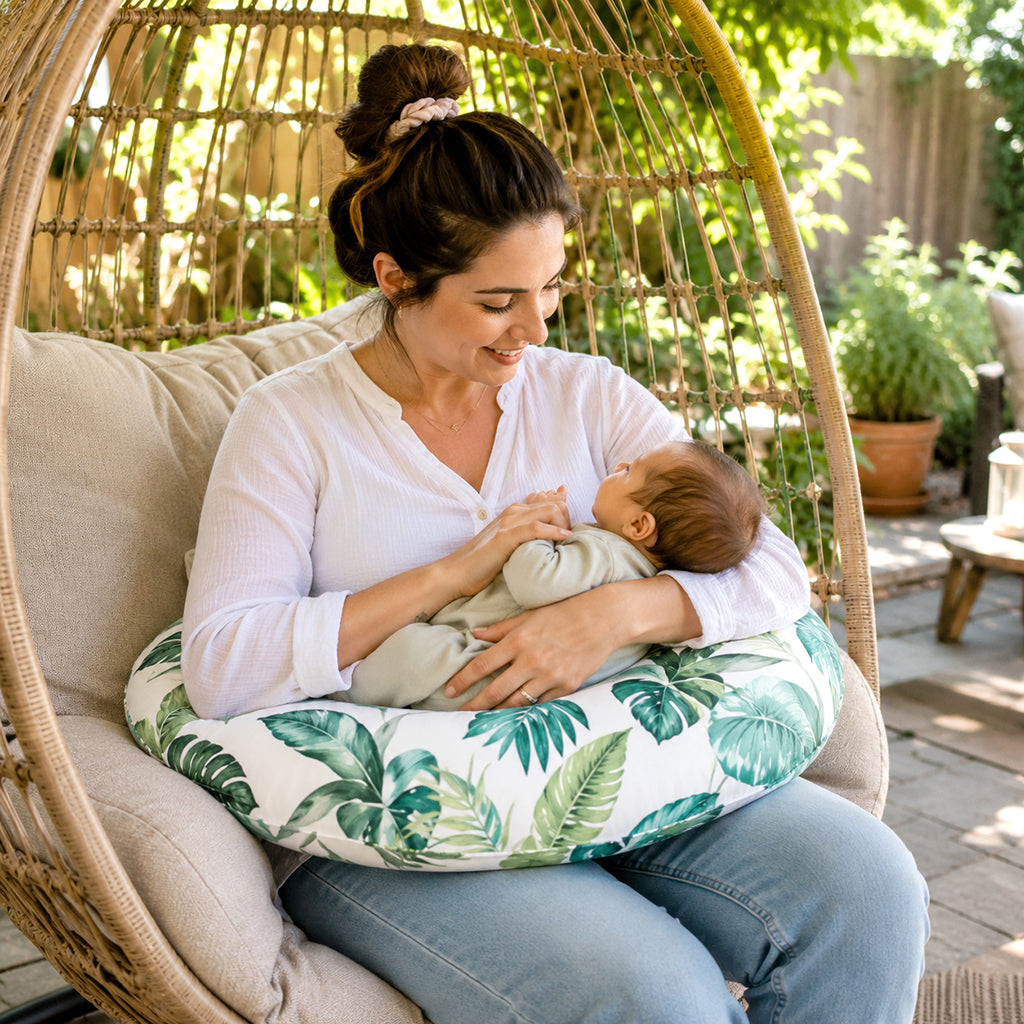 Maman assise dans le jardin avec bébé sur coussin d'allaitement