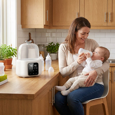 Maman donne biberon avec chauffe biberon dans la cuisine